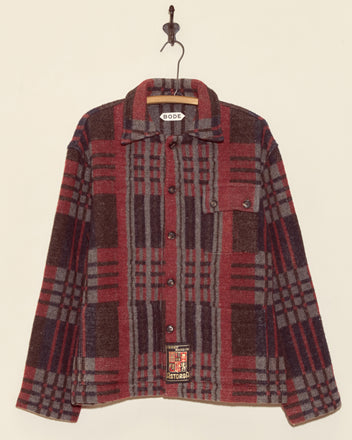 The Coniston Jacket - XS/S, a unique red and grey plaid button-up, hangs on a hook against a plain light background.
