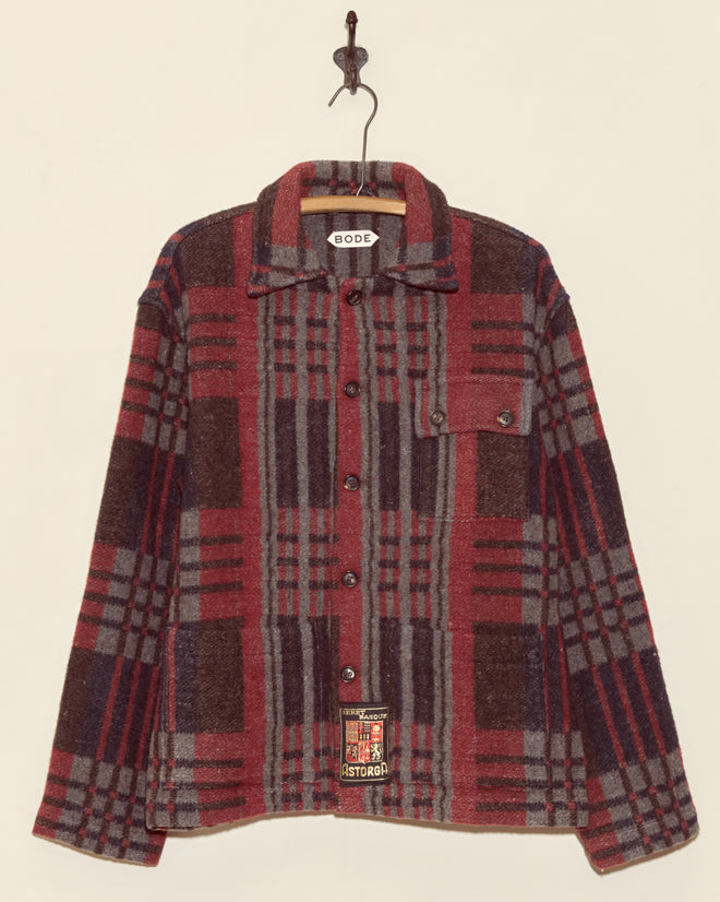 The Coniston Jacket - XS/S, a unique red and grey plaid button-up, hangs on a hook against a plain light background.