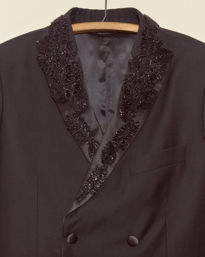 The Beaded Connaught Tuxedo Jacket is a black double-breasted blazer for men, featuring beaded leaf embroidery on satin lapels—an elegant choice for special occasions.