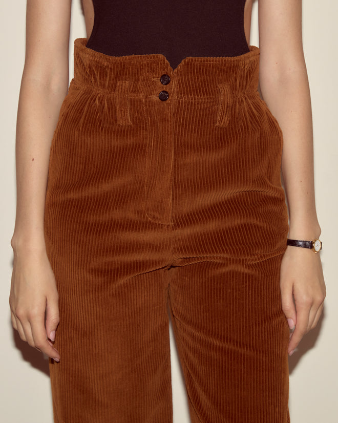Person wearing Corduroy Shakey Trousers - Brown, styled with wide legs and a high-rise fit, paired with a black sleeveless top and a wristwatch for accessories.
