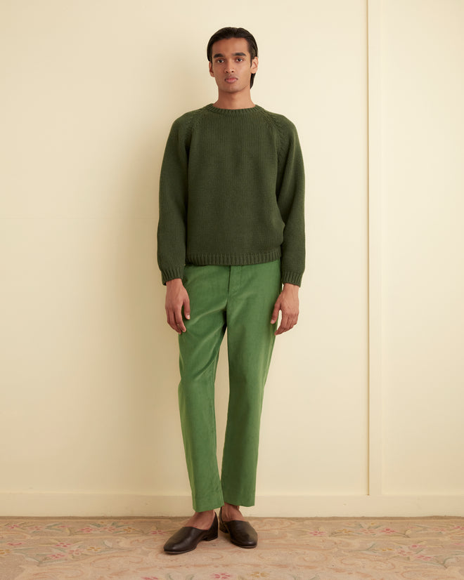 A person in a green sweater and Corduroy Side Buckle Trousers stands against a light-colored wall on a patterned carpet.