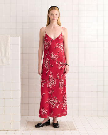 A woman stands in a white-tiled room wearing the Creeping Begonia Slip Dress and black shoes.