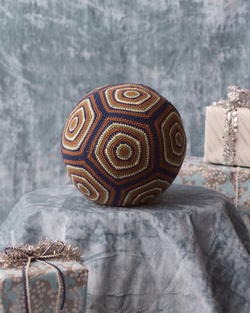 A Crochet Ball on a marbled fabric background, accompanied by wrapped presents and a cozy vintage knit pillow, creates a charming scene.