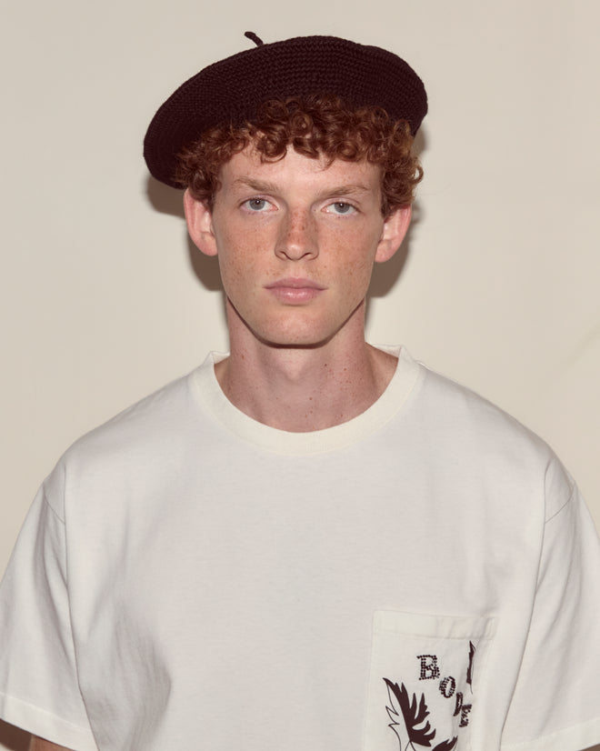 Young person with curly red hair wears a black Crochet Beret and a white t-shirt, standing against a plain background.