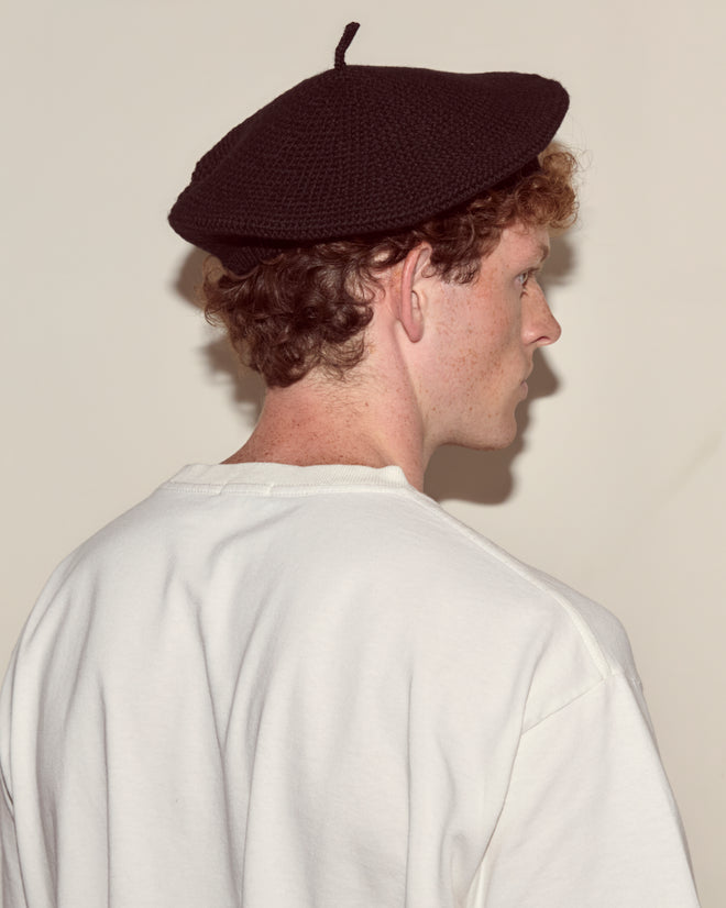 Person with curly hair wearing a Crochet Beret - Black and a white shirt, shown from behind against a plain background.