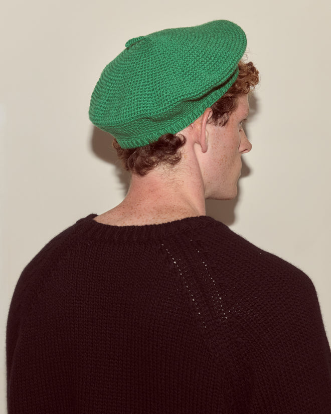 Person with curly hair wearing a green Crochet Beret and a black sweater, shown from behind—an effortlessly chic look that highlights stylish accessories.