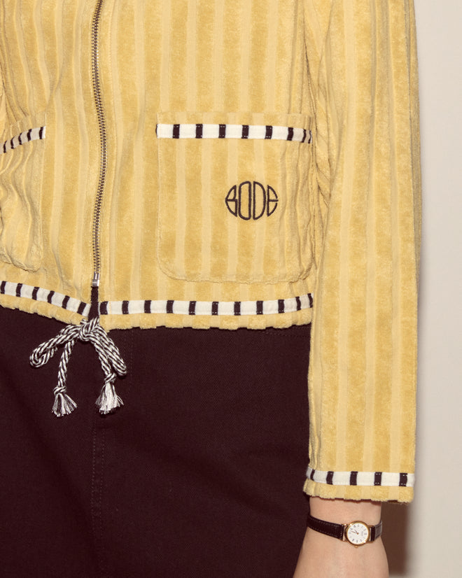 A person wearing a Croquet Ground Hoodie with yellow stripes, featuring an embroidered Bode logo, and a watch on their wrist.