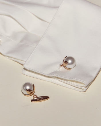 A white shirt cuff with Curio Cufflinks - White, one matching cufflink nearby featuring a gold tag engraved 