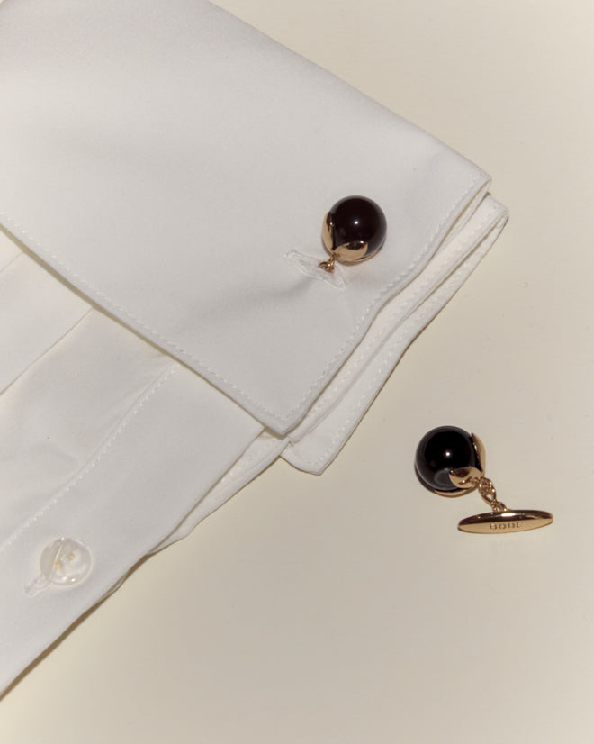 White dress shirt with Curio Cufflinks - Black—one attached to the cuff, one resting nearby on a light surface.