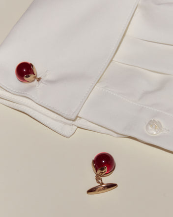 A white dress shirt with Curio Cufflinks - Red—one attached and one placed nearby—rests elegantly on a cream surface.