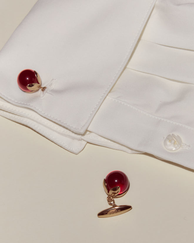 A white dress shirt with Curio Cufflinks - Red—one attached and one placed nearby—rests elegantly on a cream surface.
