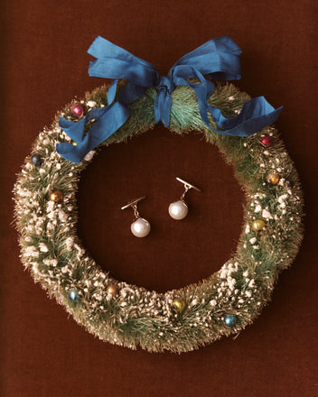 A Christmas wreath decorated with colorful ornaments and a blue ribbon features an elegant touch at its center with Curio Cufflinks – White, reminiscent of Victorian Revival charm.