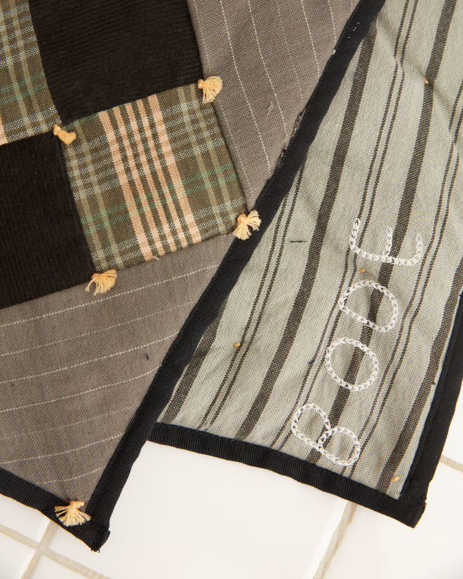 A pair of Corduroy Nine Patch Quilt Scarf pillows, with a black and green plaid design inspired by 1920s-1930s quilting, rest elegantly on a white tiled floor.