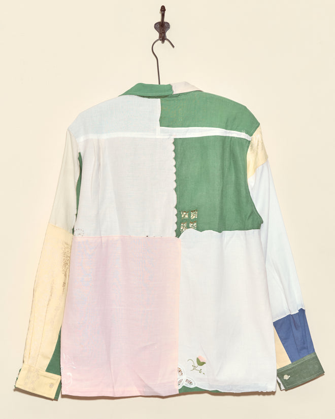 The Damask Greens Napkin Shirt - L/XL features unique pastel and green fabric squares inspired by vintage napkin shirts, displayed hanging on a wall hook with the back view shown.