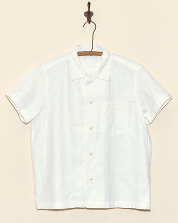 The Damask Moonflower Short Sleeve shirt, a white button-up with short sleeves, hangs on a hanger against a beige wall.