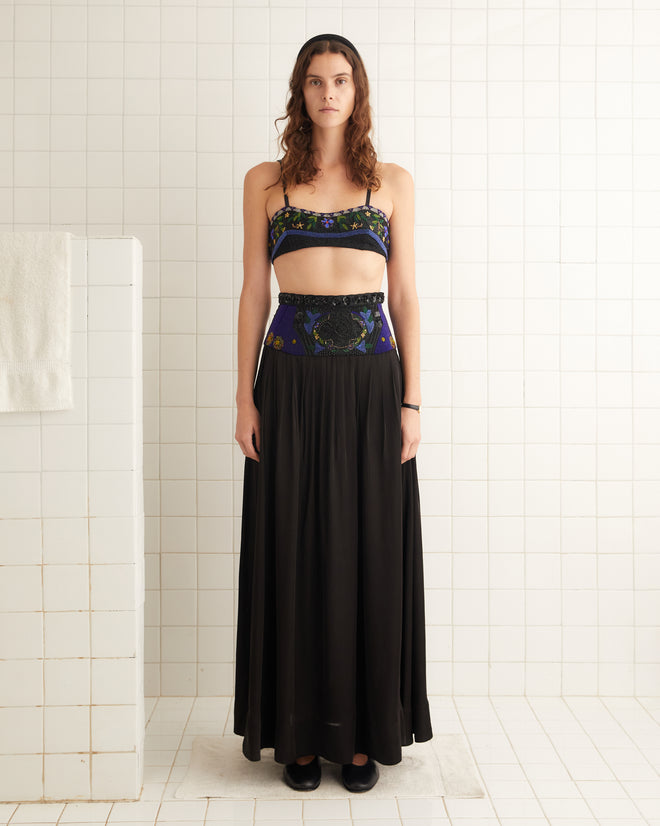 A woman in a floral bandeau top and the elegant Deco Collage Skirt stands gracefully in a tiled room.