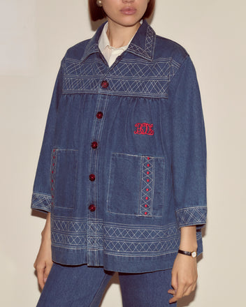 Woman wearing the Embroidered Denim Quincy Jacket by Bode, featuring red buttons and unique detailing, paired with matching denim pants.