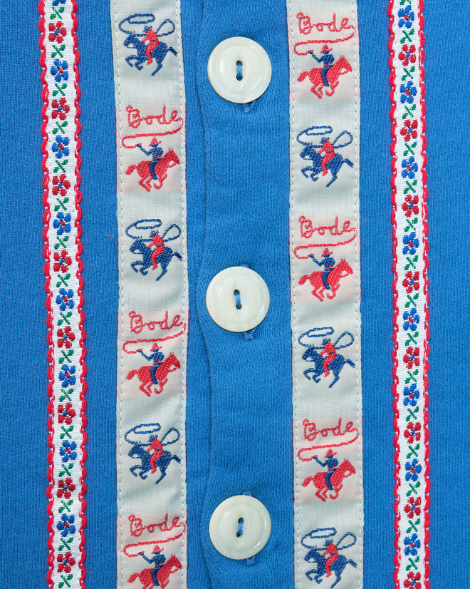 Close-up of the Ribbon Cardigan in blue 100% cotton, featuring antique pearl buttons and embroidered red and blue monkeys, text, and floral patterns.