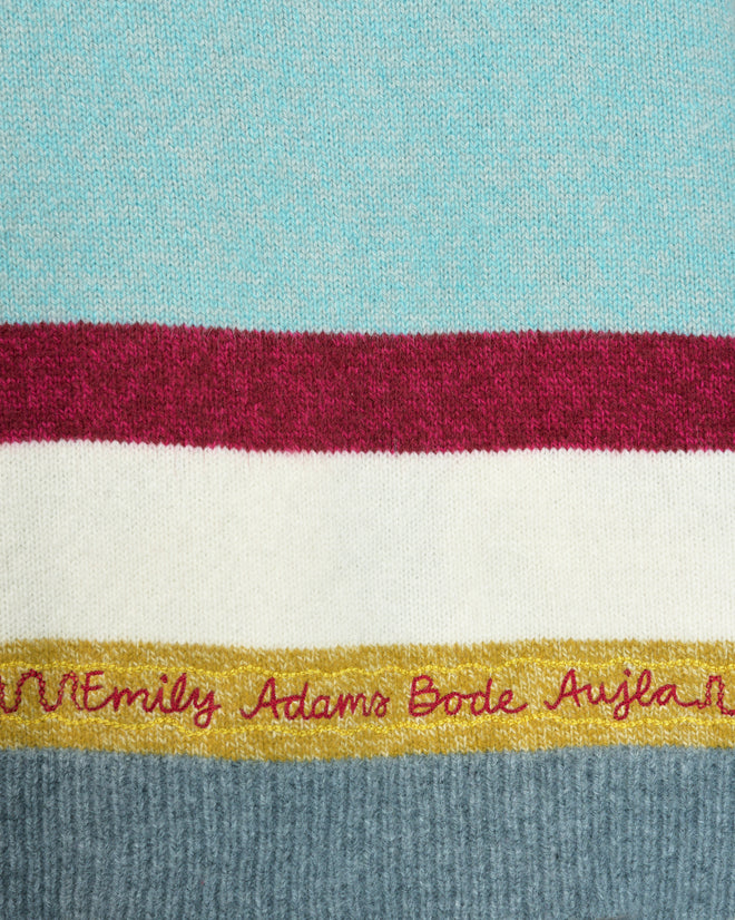 Close-up of knit fabric with colored stripes and “Emily Adams Bode Aujla” embroidered in red cursive, featuring a subtle Western yoke detail inspired by the signature Rock Candy Cardigan. Crafted from 100% wool for warmth and comfort.