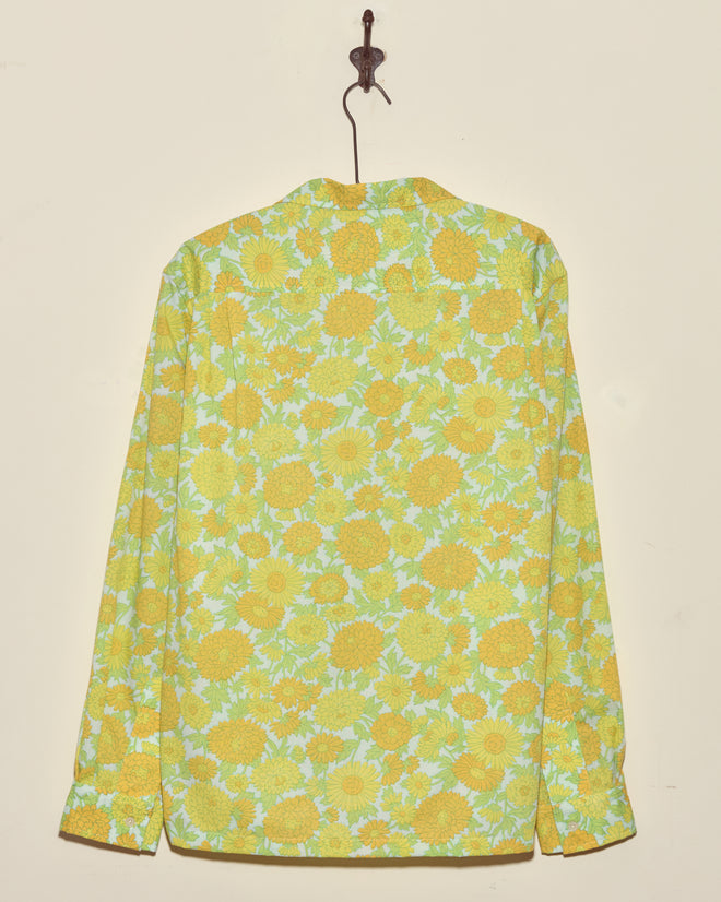 The Dhalia Lime Long Sleeve Shirt in XXL, featuring a yellow and green floral pattern, hangs on a hook against a beige wall.