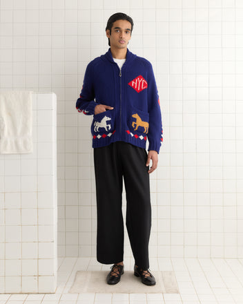 A person in a blue Diamond Corral Cardigan with animal designs, black pants, and sandals stands gracefully on a white tiled floor.