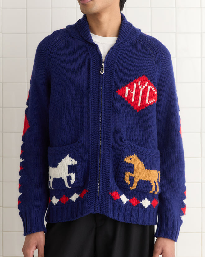 A person wearing the Diamond Corral Cardigan, designed in soft merino wool, stands against a tiled wall.