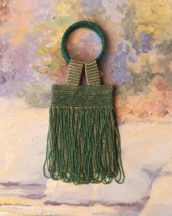 A Bracelet Evening Bag in blue and green, featuring a ring handle and fringe, is set against a colorful, textured background, capturing the allure of a 1930s reproduction.