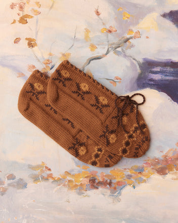 Knit Jacquard Slippers in brown, adorned with floral patterns, placed against a snowy painted backdrop.