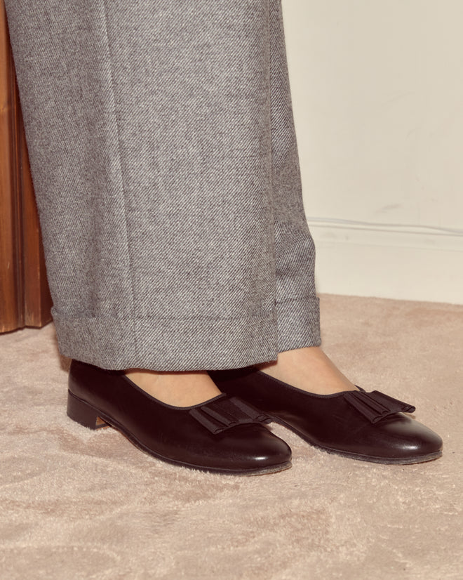 Person wearing Dovecote Port Trousers in heathered grey wool from a UK mill, paired with black bow loafers, standing on a beige carpet—a nod to timeless suiting style.