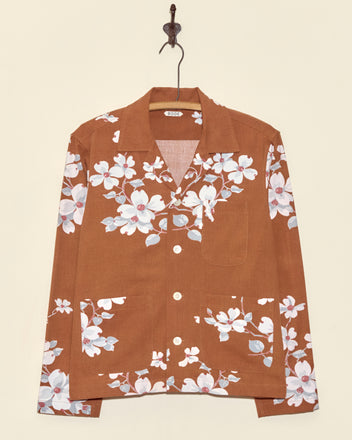 The Dogwood Bark Long Sleeve Shirt - XS is a unique brown button-up with a white and pink floral print, shown hanging on a hook against a beige wall.