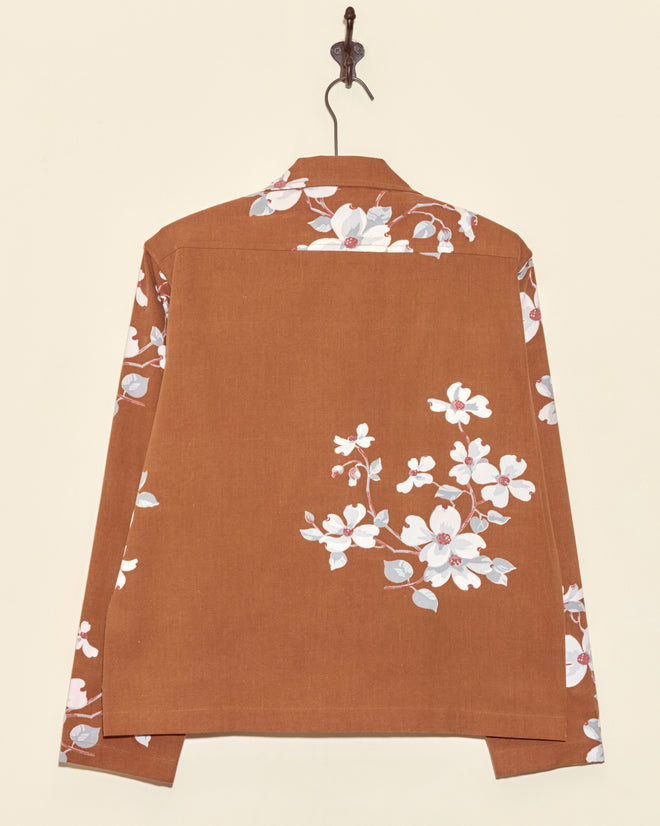 Dogwood Bark Long Sleeve Shirt (XS) in brown, featuring a unique white and pink floral print on the back, sleeves, and shoulders, hanging on a hook.