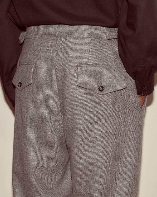 Wearing Dovecote Trousers—UK-woven grey wool with back pockets—and a black shirt, hands in pockets, for a classic suiting look.