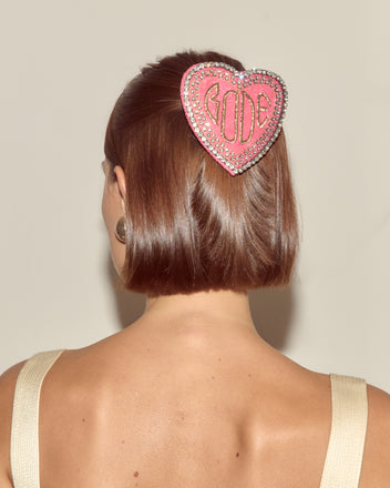Woman with a bob haircut, seen from behind, wears the Duchess Barrette—a pink, heart-shaped accessory featuring the word 