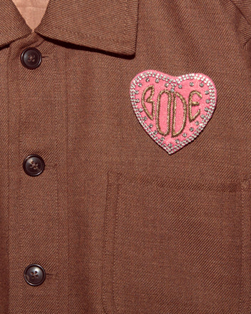 The Duchess Brooch is a brown shirt featuring a pink, heart-shaped 