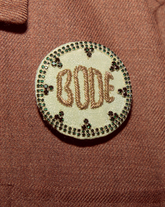 A round embroidered Willow Brooch in green on a brown textured fabric background, perfect for adding to your collection of Bode accessories.