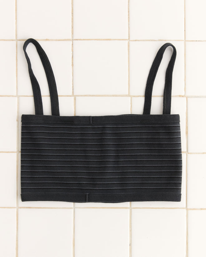 Ducky Bra in black features a ribbed bandeau design, adjustable straps, and a stylish tie-front detail on a white tile background.