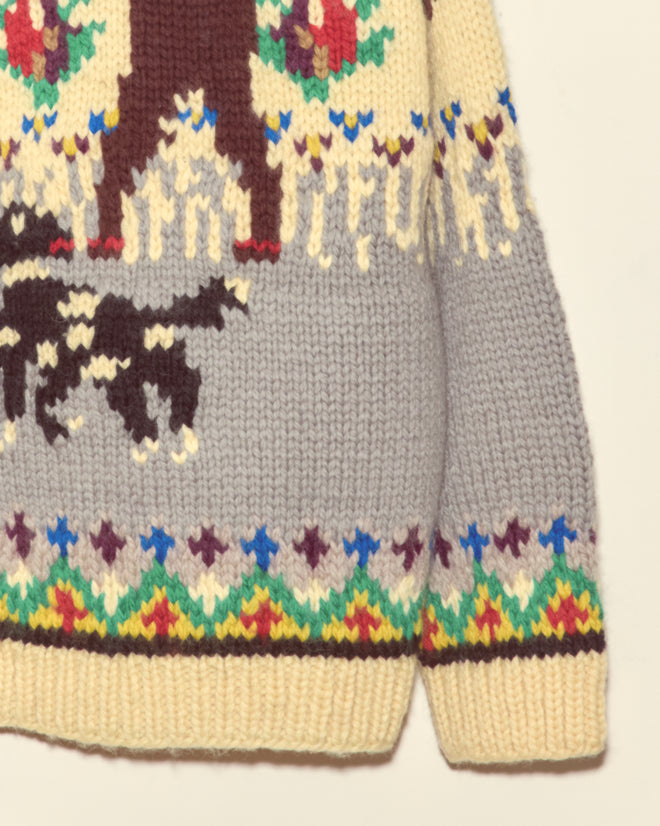 The Pheasant Cardigan is a cotton knitwear sweater with moose and dog patterns and colorful geometric designs along the hem, capturing vintage 1960s charm.
