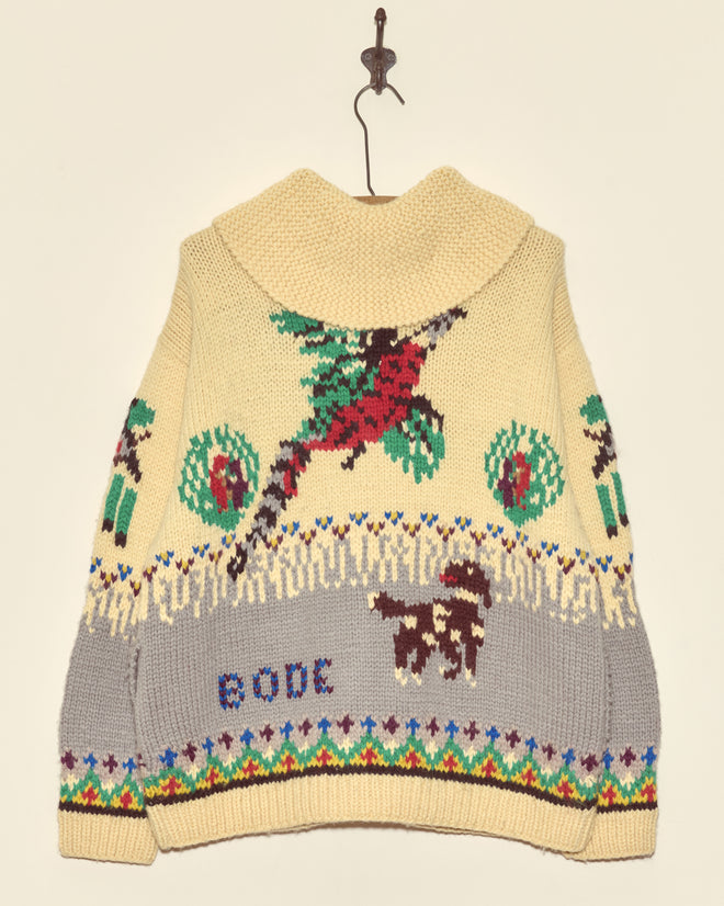 The Pheasant Cardigan is a cream cotton knit sweater featuring colorful bird, dog, and tree patterns inspired by 1960s cardigans, with 