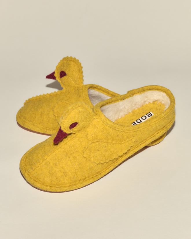 The Duck Slipper - Yellow Red features cute, fleece-lined slippers designed to look like ducks, with wings, eyes, and beaks on a neutral background.