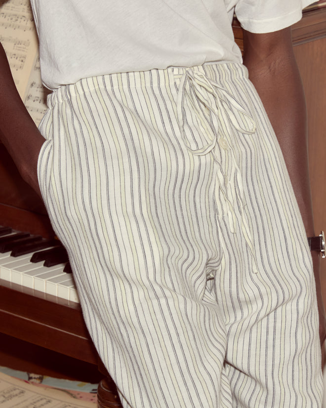 Person in a white shirt and Electric Light Pajama Pants with an adjustable drawstring waist stands by a piano, sheet music in the background.