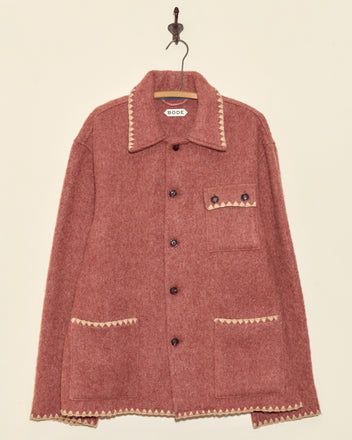 The Ember Crackle Jacket - XXL is a unique pink wool jacket with cream trim, a button front, and three pockets, displayed on a wall hook.