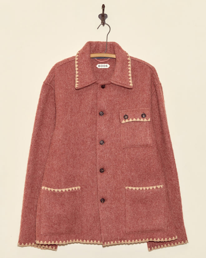 The Ember Crackle Jacket - XXL is a unique pink wool jacket with cream trim, a button front, and three pockets, displayed on a wall hook.