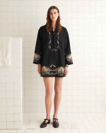 Wearing the elegant Embroidered Corsage Dress, a person stands gracefully on a white tiled floor, complemented by black shoes.