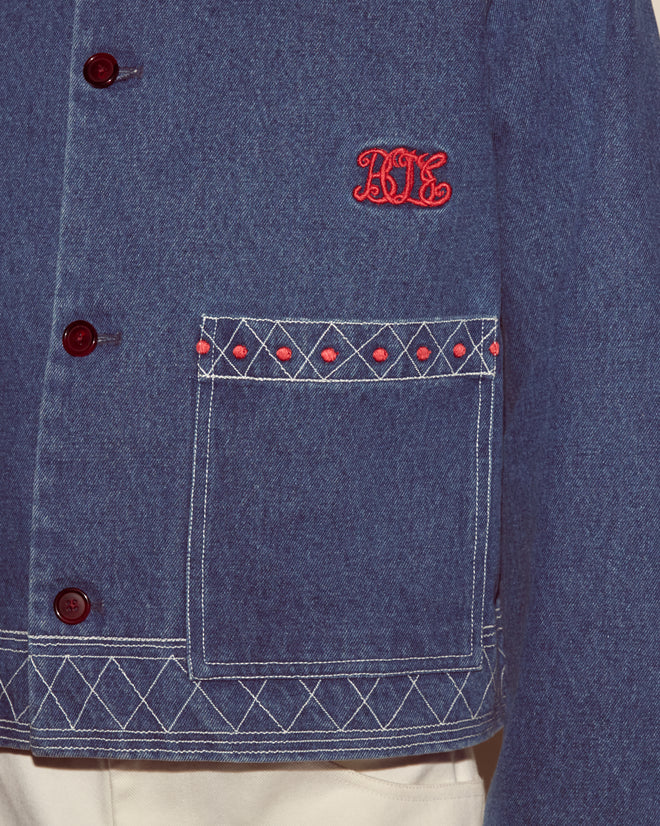 The Embroidered Denim Jacket features vintage denim, white stitching, red buttons, and bold red 