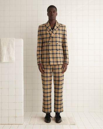 A person in the Equestrian Suit Jacket, featuring a beige and navy checkered wool design, stands against a tiled wall, highlighting the classic elegance of windowpane twill crafted by a renowned British mill.