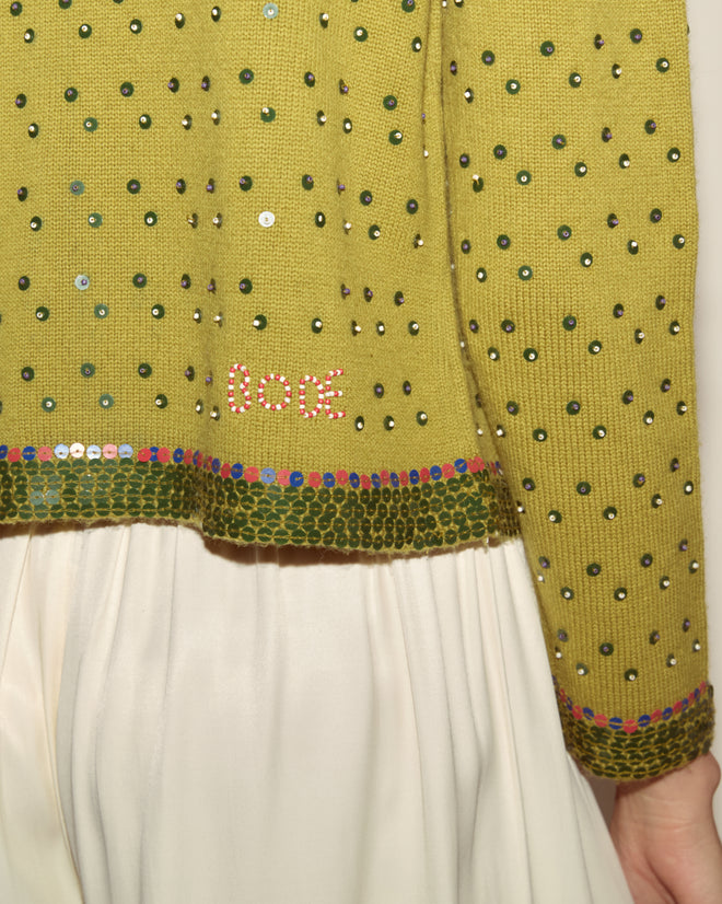 The Fairyfloss Cardigan is a green beaded sweater with “DCC” in pink beads and delicate beaded floral appliqué, styled with a white skirt.