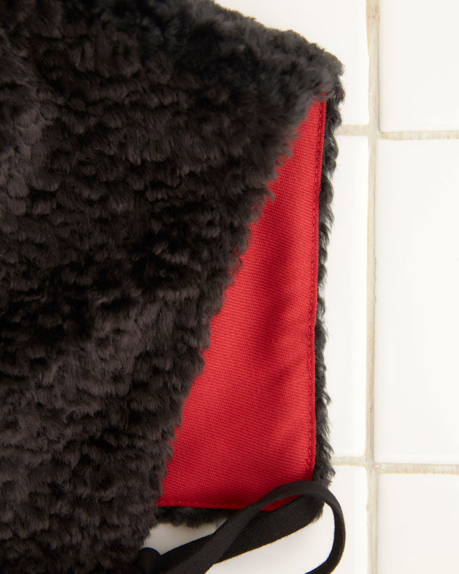 Close-up of the Faux Fur Tie Cap - Black with a red lining, made from polyester, placed on a light tiled surface.