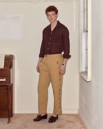 A man in a dark shirt and Feather Runner Trousers stands indoors by a piano and window, looking at the camera.