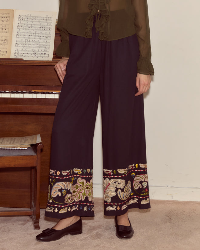 A person in Feather Runner Pants - Multi and black shoes stands by a piano with sheet music.