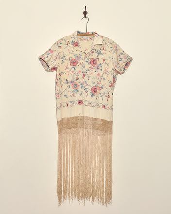 The Festival Blossom Tunic - S is a short-sleeved floral shirt dress with long beige fringe inspired by an antique piano shawl, displayed on a hanger for a unique look.